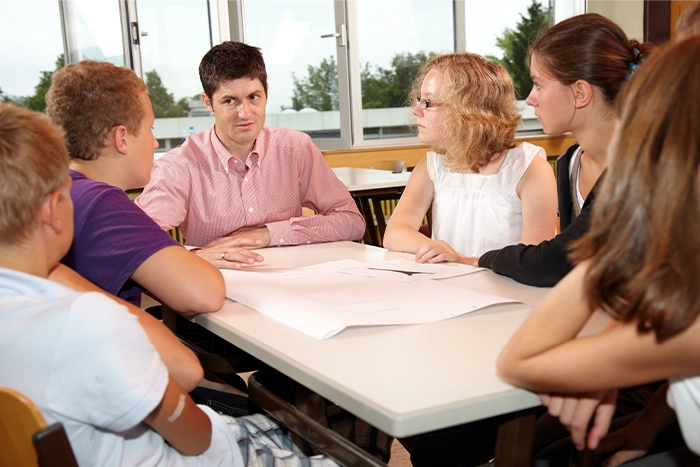 Fünf Schülerinnen und Schüler sitzen gemeinsam mit ihrem Lehrer an einem Tisch. 