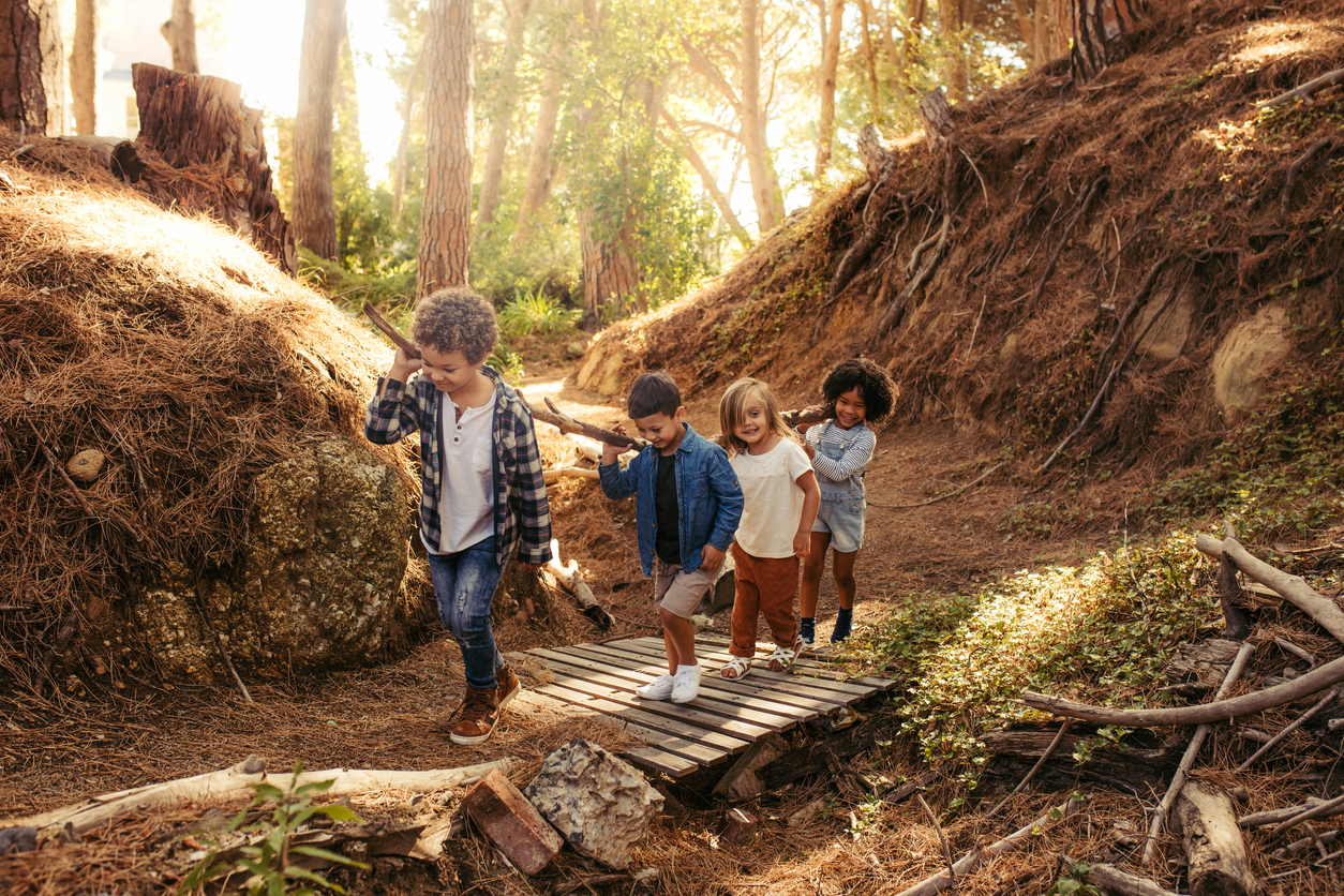 Vier Kinder laufen über eine kleine Brücke im Wald.