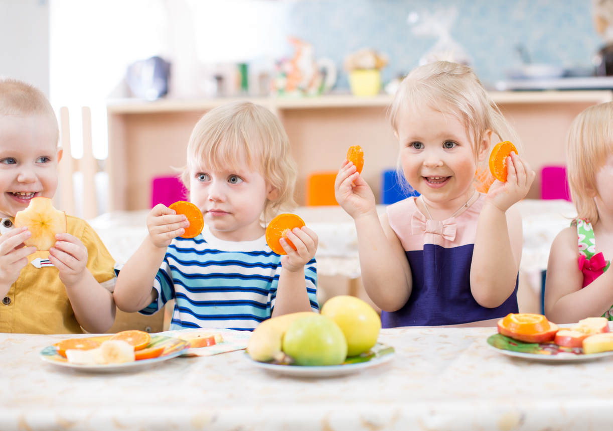 Kinder sitzen an einem Tisch und essen Obst.