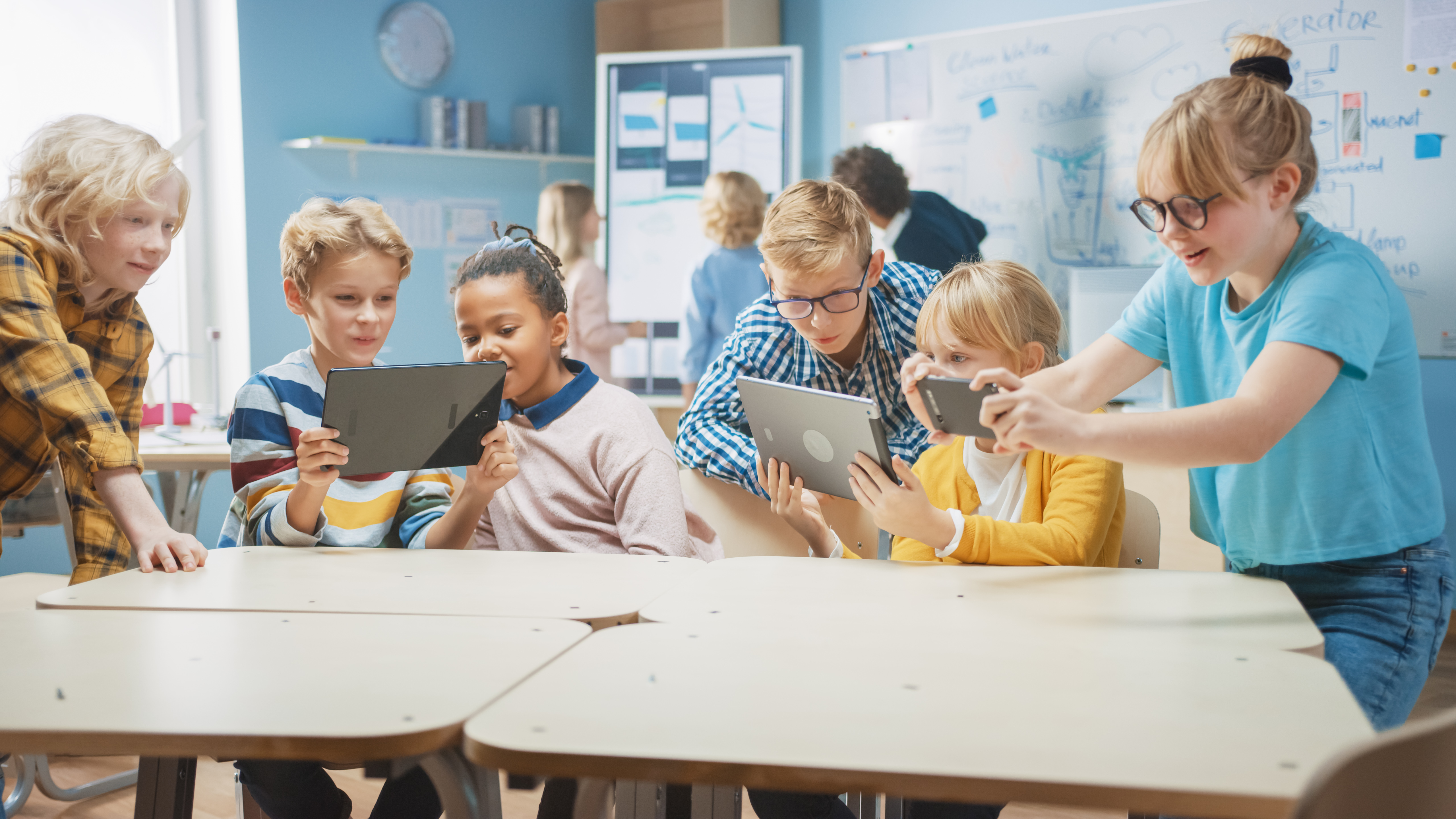 Mehrere Kinder sind in einem Klassenraum und benutzen Tablets.